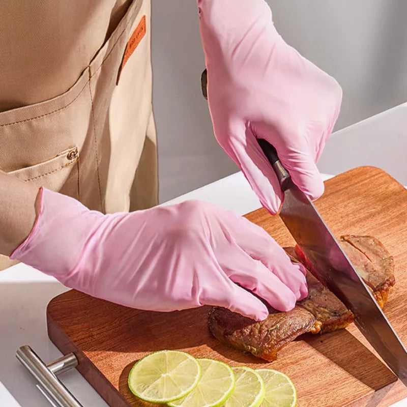 A hand wearing a pink disposable nitrile glove cuts meat on a wooden board with a knife and lime slices.