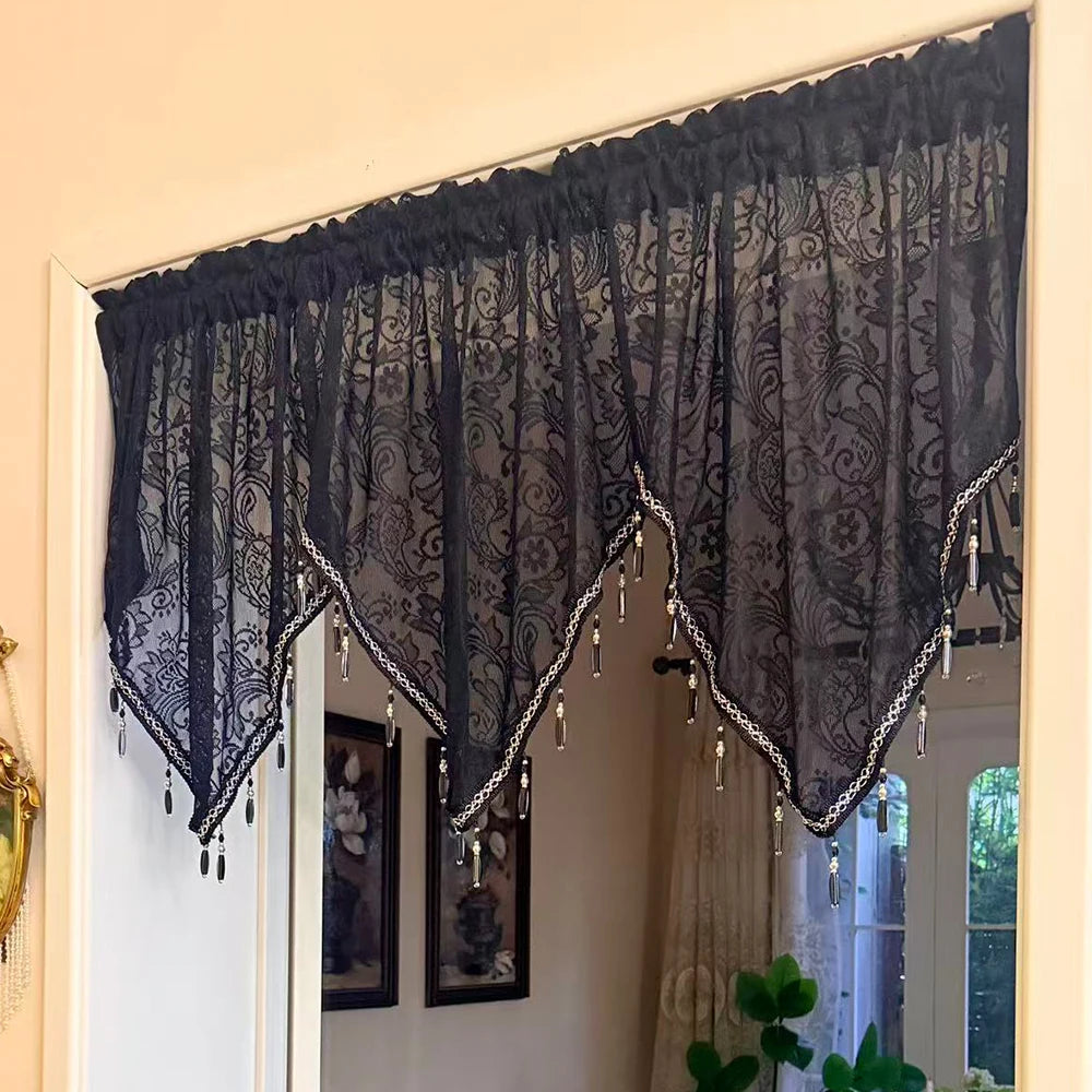 Black gothic lace curtain valance with silver fringe and tassels hanging over a window.