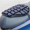 A close-up view of a black ergonomic motorcycle seat cushion with a textured surface mounted on a gray and blue seat.