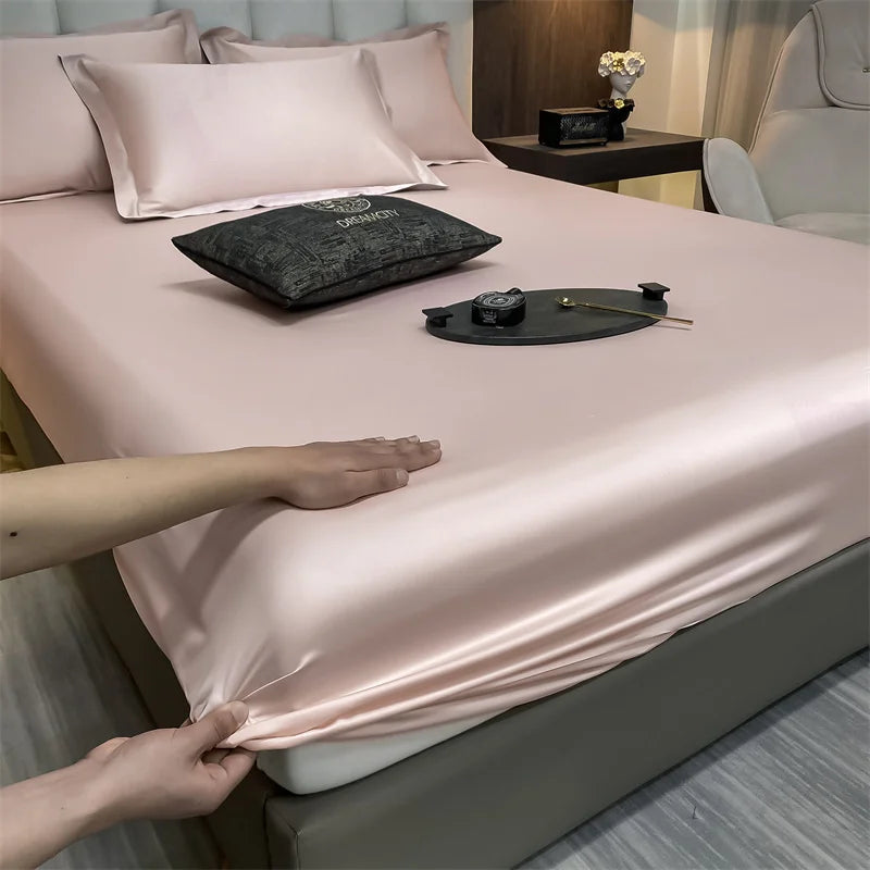 Un juego de sábanas ajustadas de algodón rosa de lujo se muestra en una cama con almohadas y un accesorio oscuro.