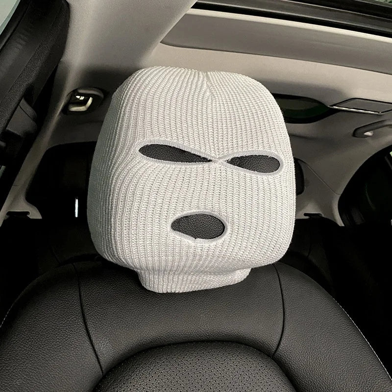 A white knitted ski mask car headrest cover placed on a black car seat.