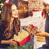 A woman holds a red box of hexagon glass honey jars with wood dippers and bee pendants in a festive setting.