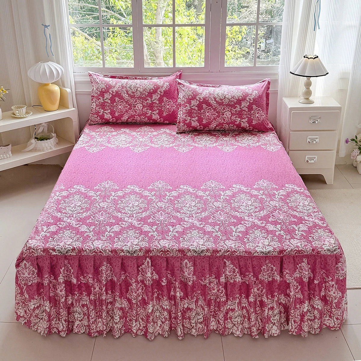 Pink floral print bed skirt and pillowcase set displayed on a bed in a bright room.