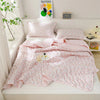 A pink floral quilted blanket is displayed on a bed with matching pillows and a sign for a summer blanket.
