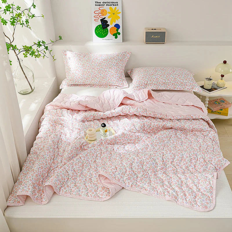 A pink floral quilted blanket is displayed on a bed with matching pillows and a sign for a summer blanket.