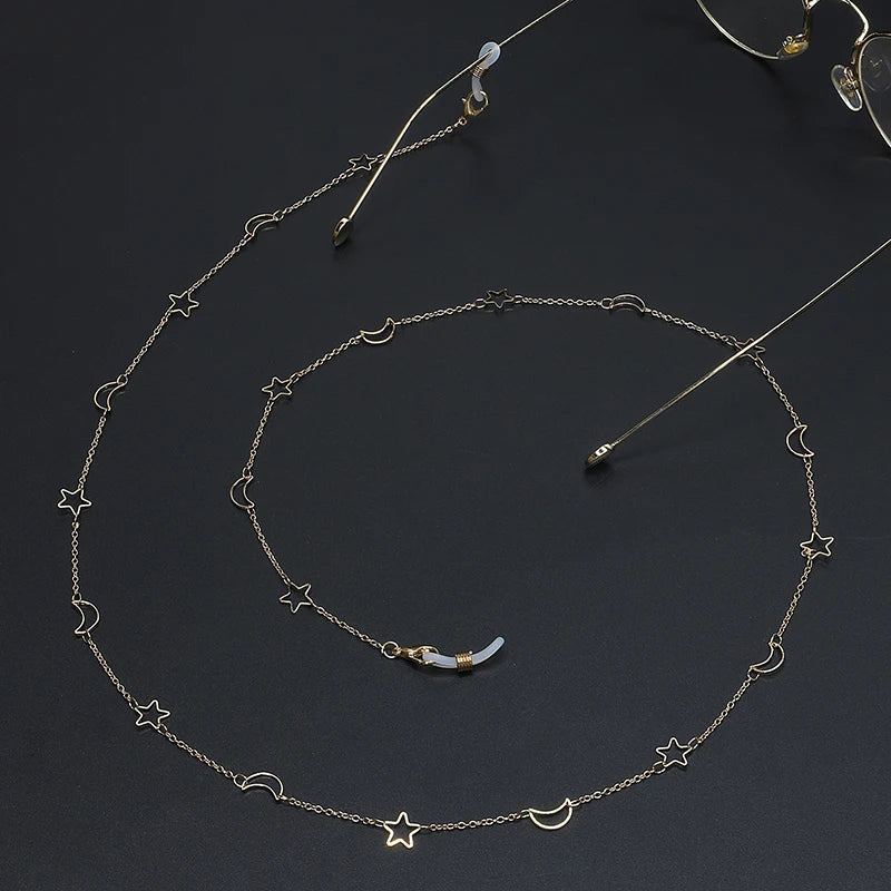 Gold chain necklace featuring a star and moon pendant, displayed against a dark background.
