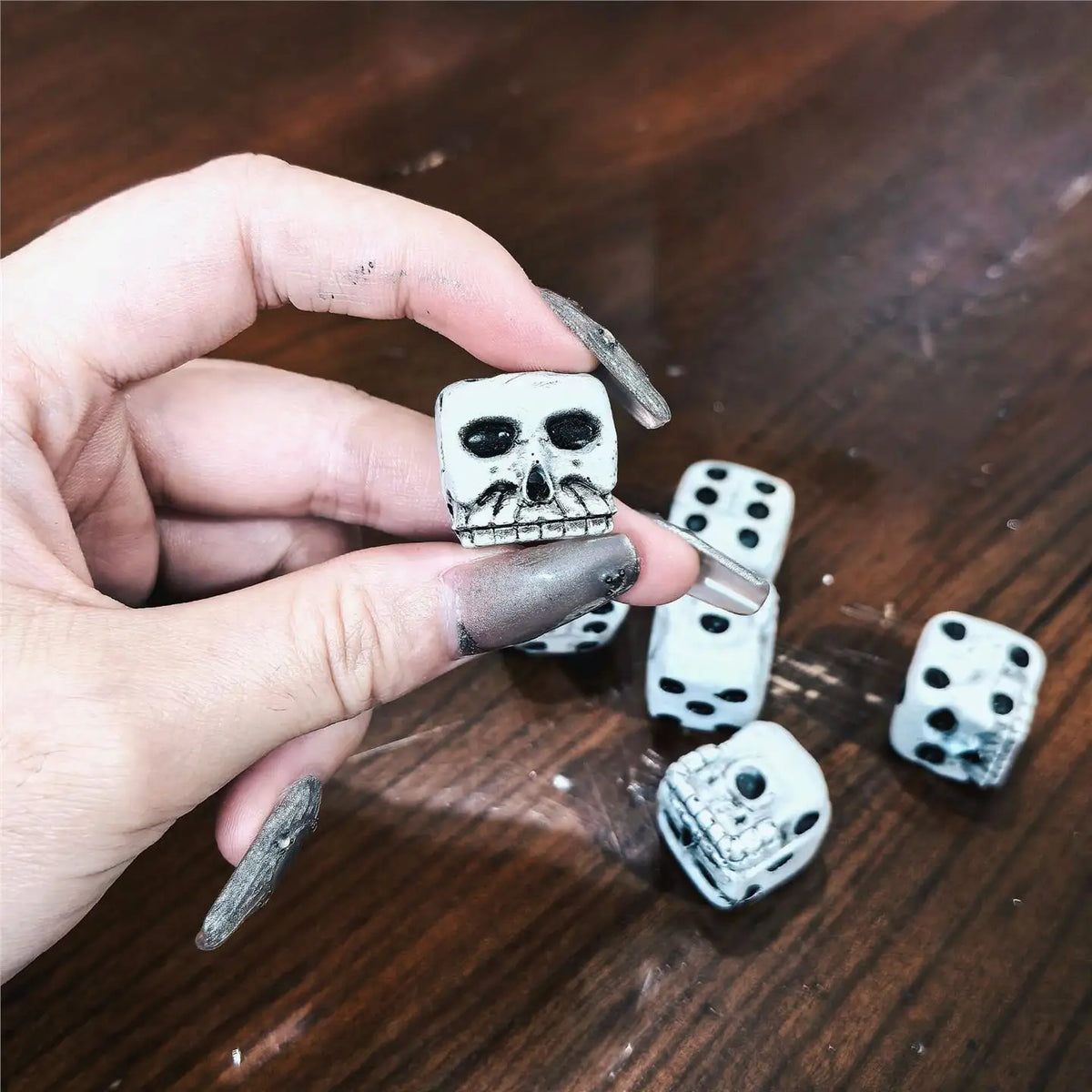 A hand holds a skull-themed dice set featuring a skull and various dice on a wooden surface.