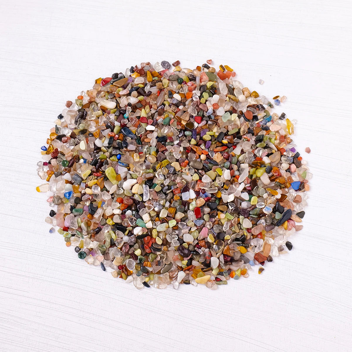 A pile of mixed natural crystal gravel stones and gemstone chips in various colors like amber, red, green, and brown.