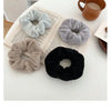 Three plush coil hair ties in gray, beige, and black resting on an open book next to a wooden mug.