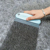 A hand is using a light blue pet hair removal brush on a gray, textured surface.