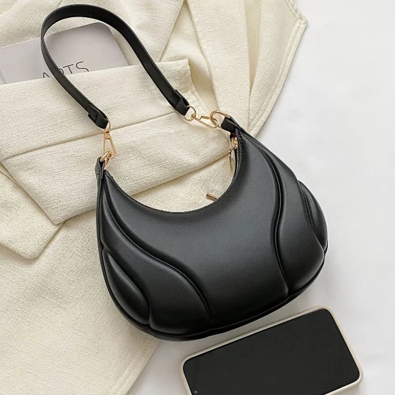 A black textured crossbody bag with a gold-toned adjustable strap resting on a light beige fabric.