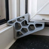 A gray heavy-duty non-slip door stopper wedge is shown installed in a white window frame.