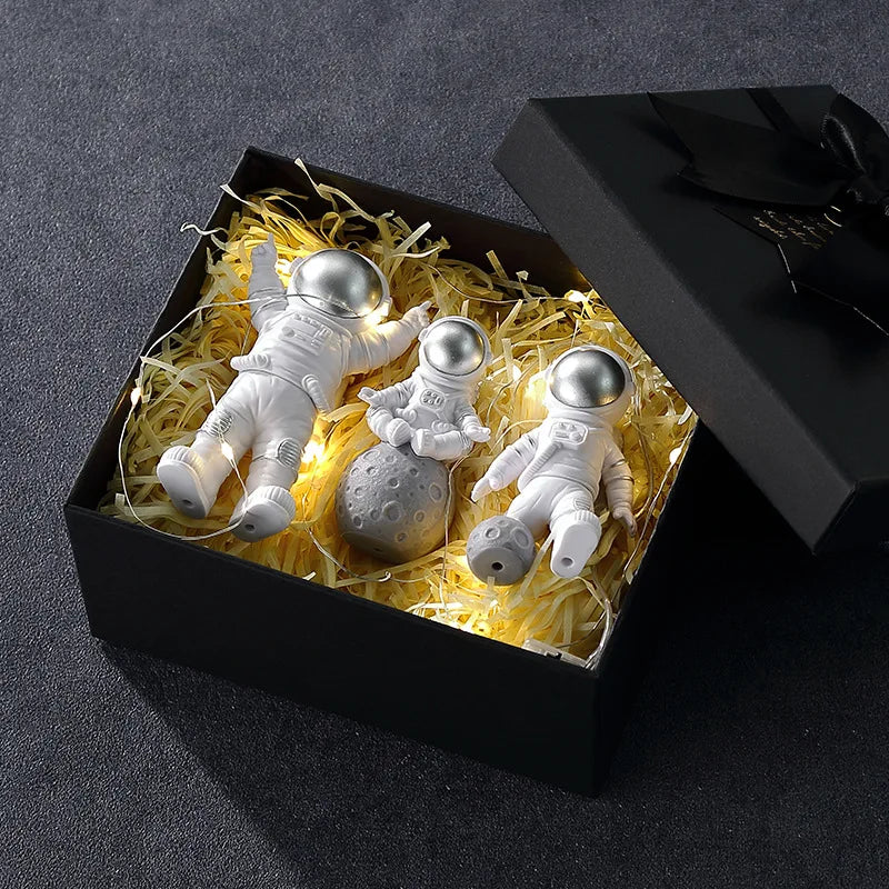 A black box contains three handcrafted astronaut figurine resin spaceman desk decor figures nestled in yellow straw.