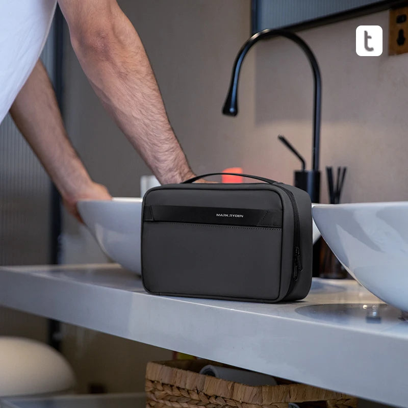 A dark gray waterproof travel toiletry bag is placed on a white counter next to a sink.
