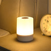 A white LED table lamp with a warm glow illuminates a bedside surface next to an analog clock.