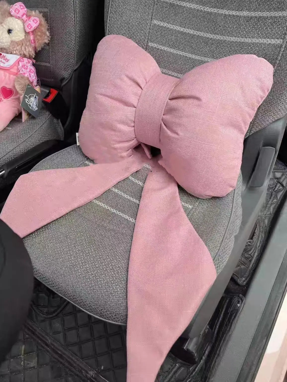 A pink butterfly bow tie neck pillow with a matching fabric cover is shown on a gray chair.