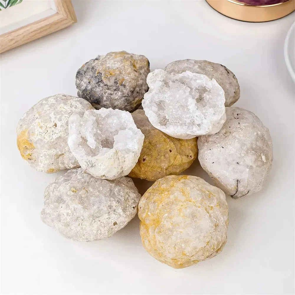 A cluster of natural agate geode crystals in various shades of gray, white, and yellow resting on a white surface.