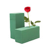 A green floral foam square with a red rose and green leaves growing out of it.