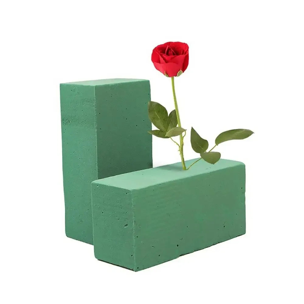 A green floral foam square with a red rose and green leaves growing out of it.