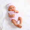 A realistic baby doll with pink clothing and a matching hat lying on a white surface.