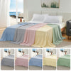 A display of various colored ice silk blankets draped on a bed, showing shades of blue, gray, pink, yellow, and green.