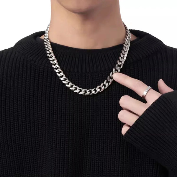 Gros plan d'un collier Cuban link en acier inoxydable porté autour du cou sur un pull noir.