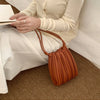 A woman holds an elegant pleated faux leather crossbody bag in a warm brown color next to white pants.