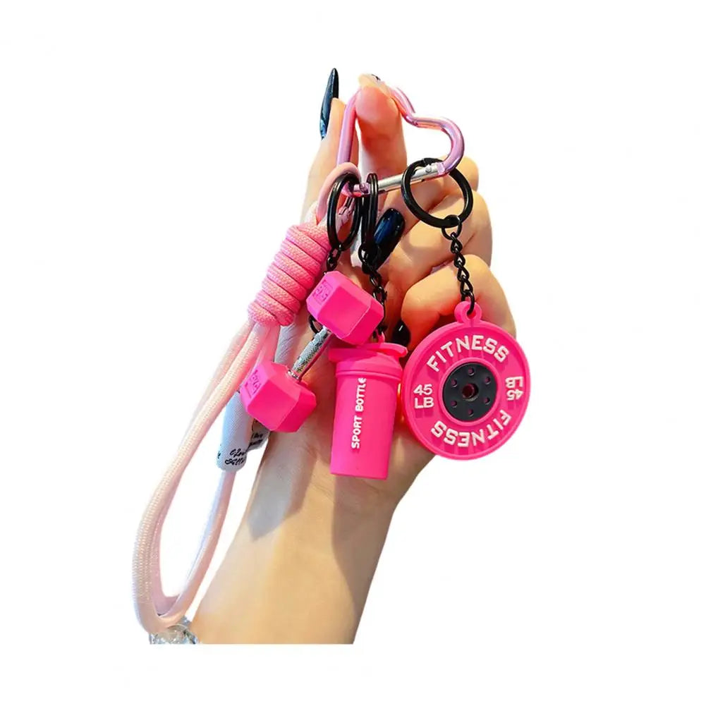 A hand holds a pink fitness keychain featuring a pink strap and multiple pink and black charms.