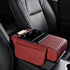 A maroon car armrest cushion with a textured cover and integrated cupholders and storage is placed on a black car seat.