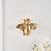 Golden bee-shaped resin wall decor mounted on a white wall.
