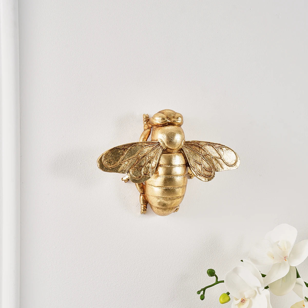 Golden bee-shaped resin wall decor mounted on a white wall.
