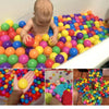 A large quantity of colorful soft play balls in various bright colors are visible in a white tub and in a hand.