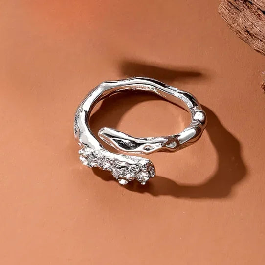 A silver irregular heart-shaped ring resting on a smooth, terracotta-colored surface.