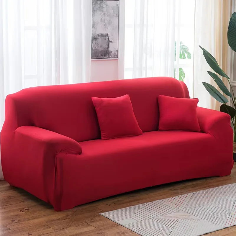 A vibrant red elastic stretch sofa cover for a 3-seater sofa with two accent pillows, placed in a bright room.
