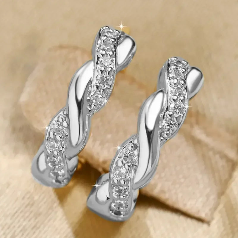 Un par de aretes de aro plateados con diseños trenzados y piedras de circonita cúbica clara.