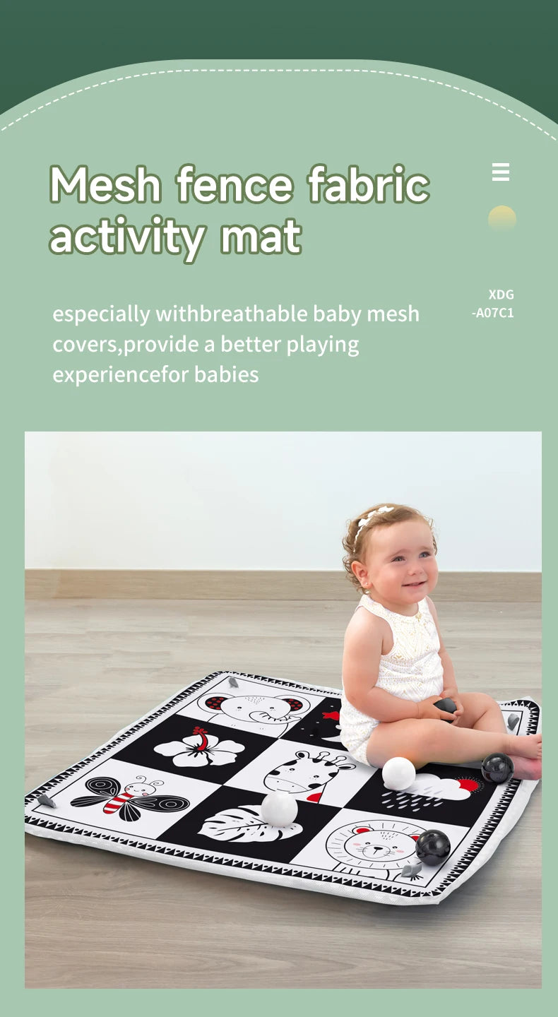A baby is playing on a black and white mesh fabric activity mat with various hanging toys.