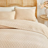 Beige plaid queen bedspread set with matching pillow shams displayed on a light wood headboard.