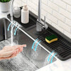 A hand is washing food under a kitchen sink splash guard, demonstrating the product's function.