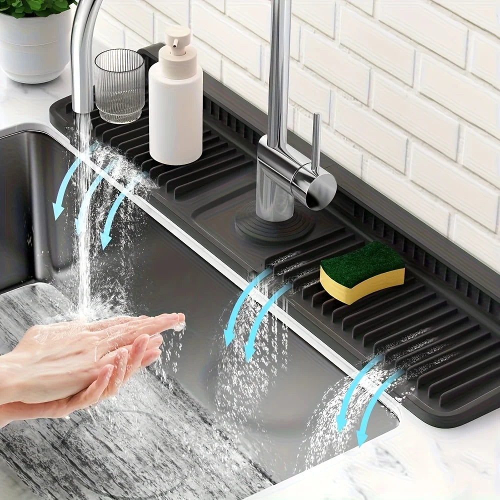 A hand is washing food under a kitchen sink splash guard, demonstrating the product's function.