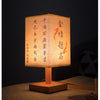 A traditional Chinese style table lamp with a light-colored linen shade displaying vertical calligraphy on a dark background.