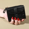 A hand holds a black PU leather wallet with a flap and zipper on a beige background.