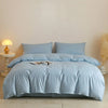 Light blue quilted duvet cover set displayed on a bed with white bedside table and natural light.