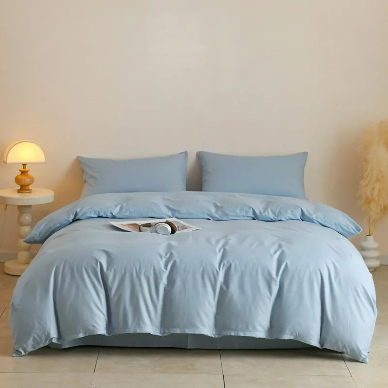 Light blue quilted duvet cover set displayed on a bed with white bedside table and natural light.