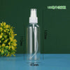 A clear glass spray bottle with a white pump dispenser and a white cap, shown next to a green plant.