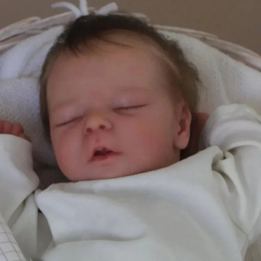 A close-up photo of a lifelike 18 inch sleeping reborn baby doll with painted veins and a soft cloth body.