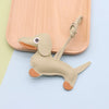 A tan PU leather dachshund puppy keychain with an ear tag and leather strap resting on a light wooden surface.