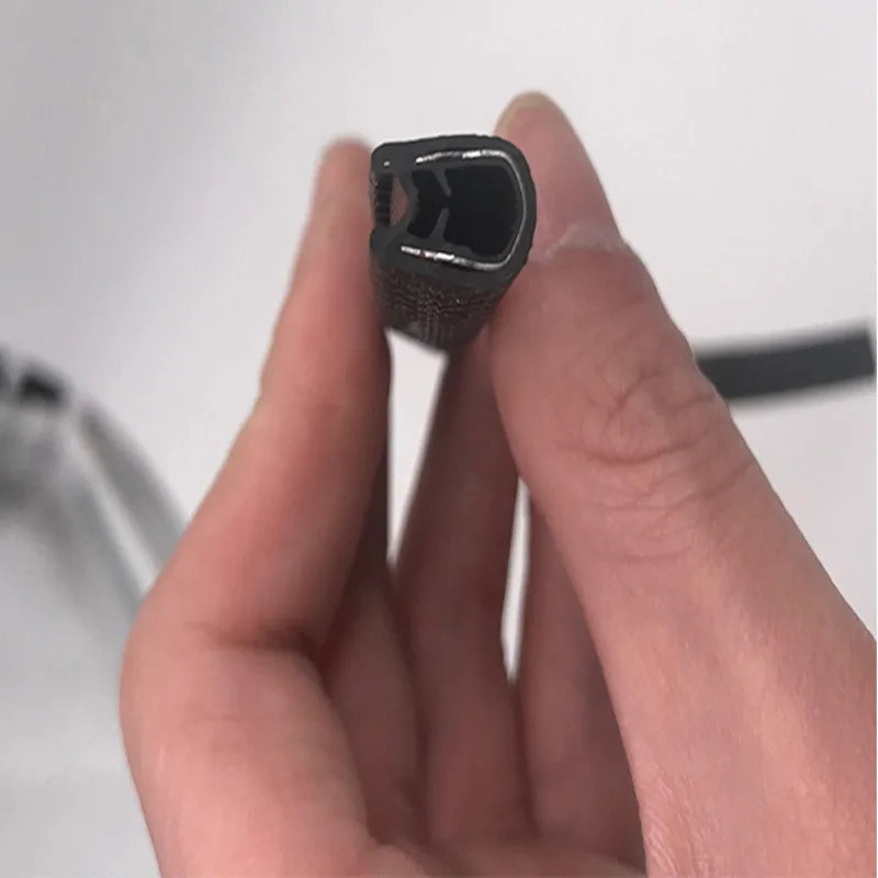 A hand holds a black U-shaped rubber edge trim with a metal core for automotive applications.