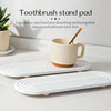 A white toothbrush stand pad with a wooden brush resting on it, displayed on a white tray.