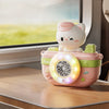 A pink camera-shaped automatic bubble machine with a white cat figure sits on a wooden surface next to a window.