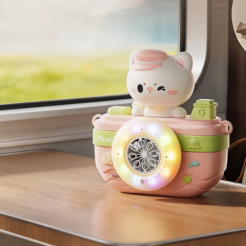 A pink camera-shaped automatic bubble machine with a white cat figure sits on a wooden surface next to a window.
